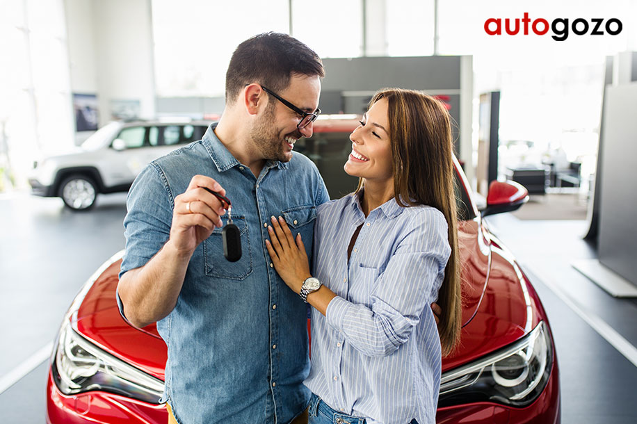 Pareja feliz mirándose frente a un coche nuevo en una concesionaria